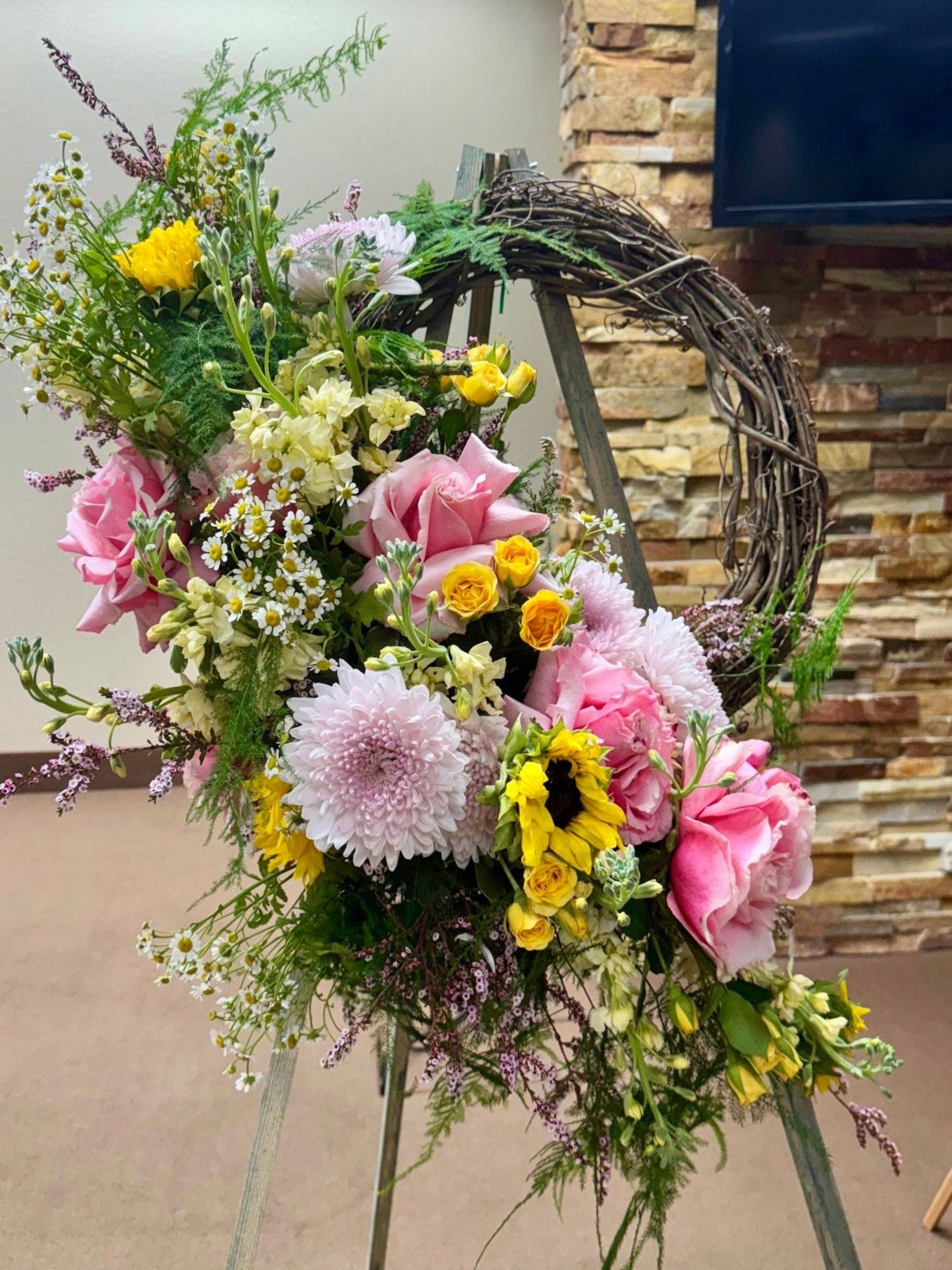 Funeral Floral arrangement on a stand with a stone wall background